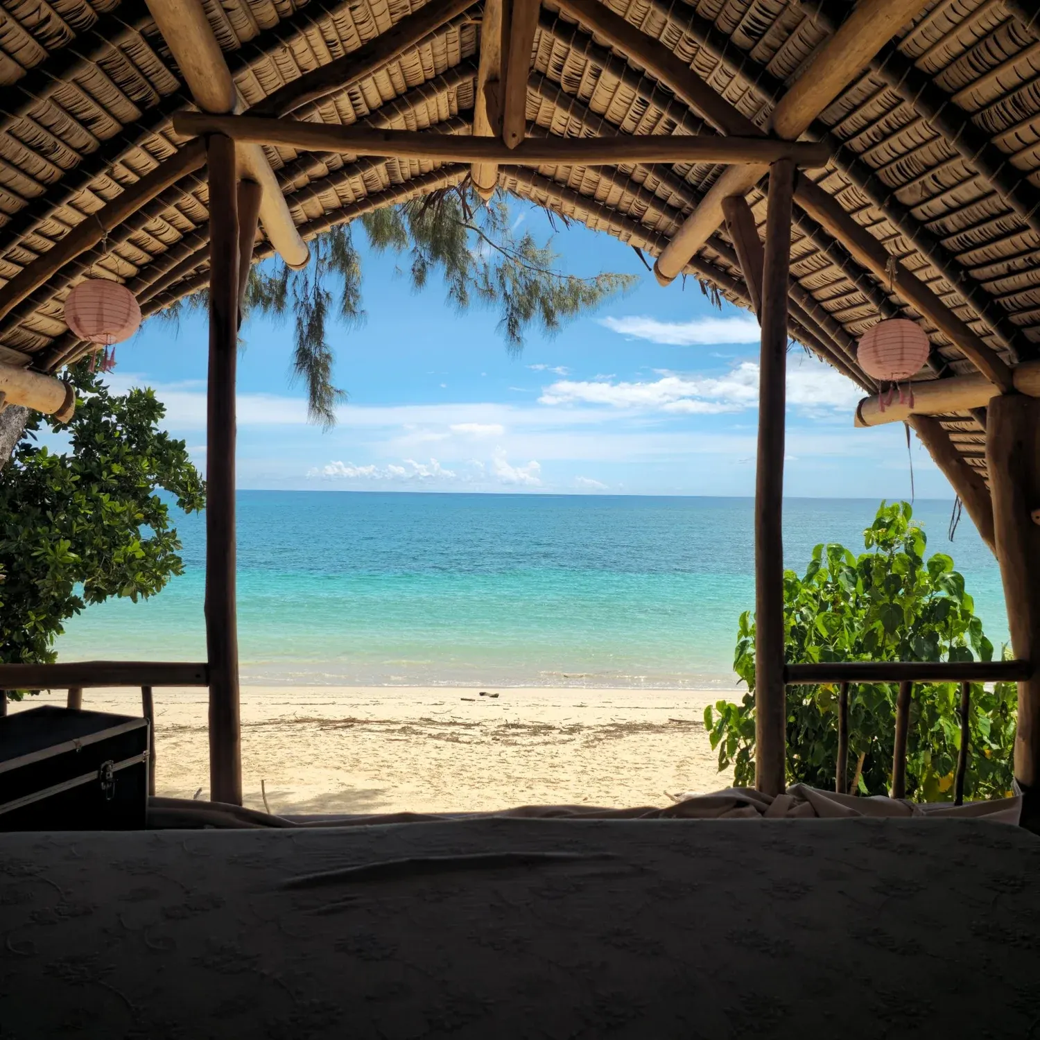 Blick vom Spirit Beach Bed durch das Palmdach auf den türkisblauen Indischen Ozean