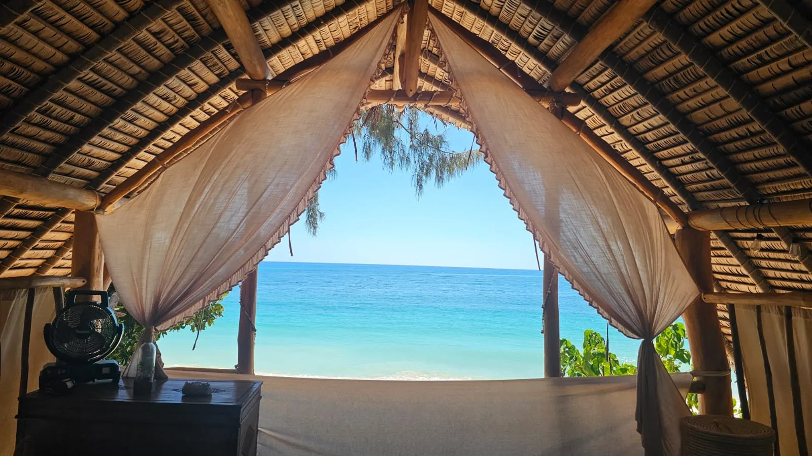 Blick vom Spirit Beach Bed durch die weißen Vorhänge auf den türkisblauen Indischen Ozean